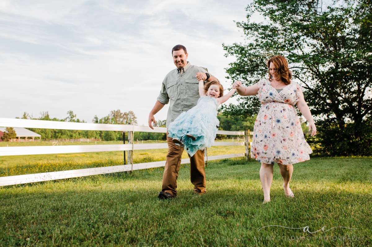 parents swinging toddler by the arms as they walk through a field, photographed by anika colombo photography
