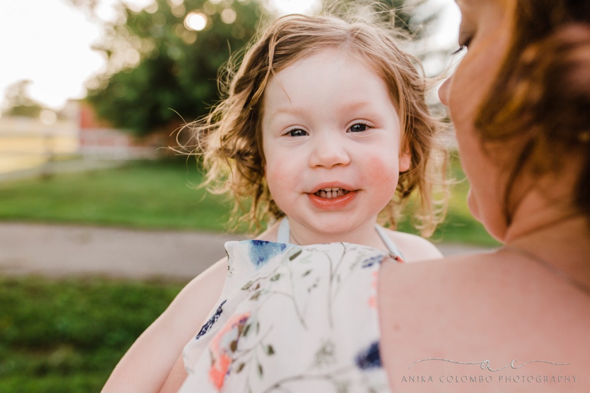 toddler staring into the camera over her mother's shoulder giggling