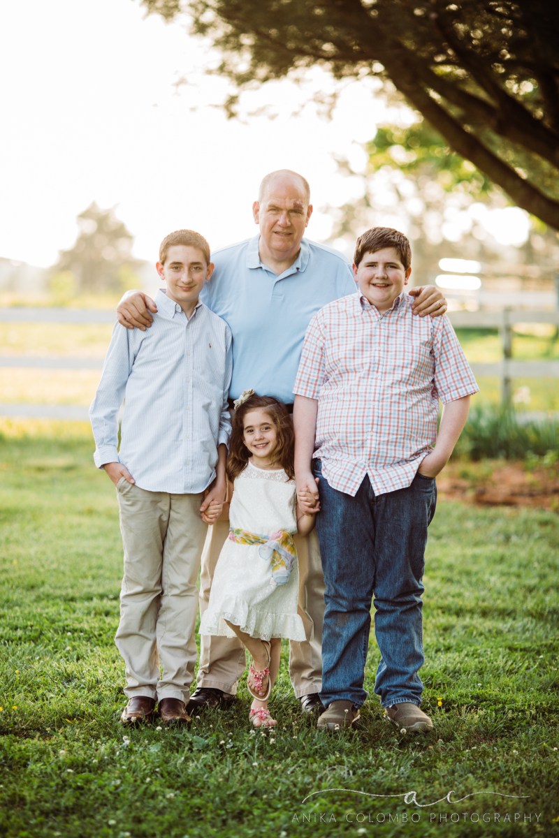 father standing in a field holding his sons by the shoulders with young daughter standing between them holding her brothers hand