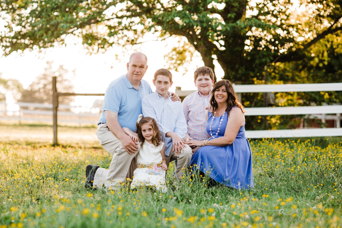 family kneeling in a field of buttercups backlit with the sun peeking through the trees