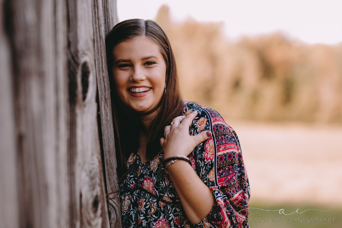 young girl leaning against an old wooden barn laughing at the camera
