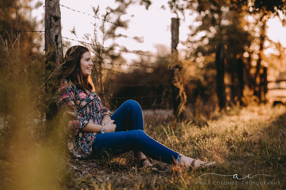 young girl in a field against a fence smiling into the distance