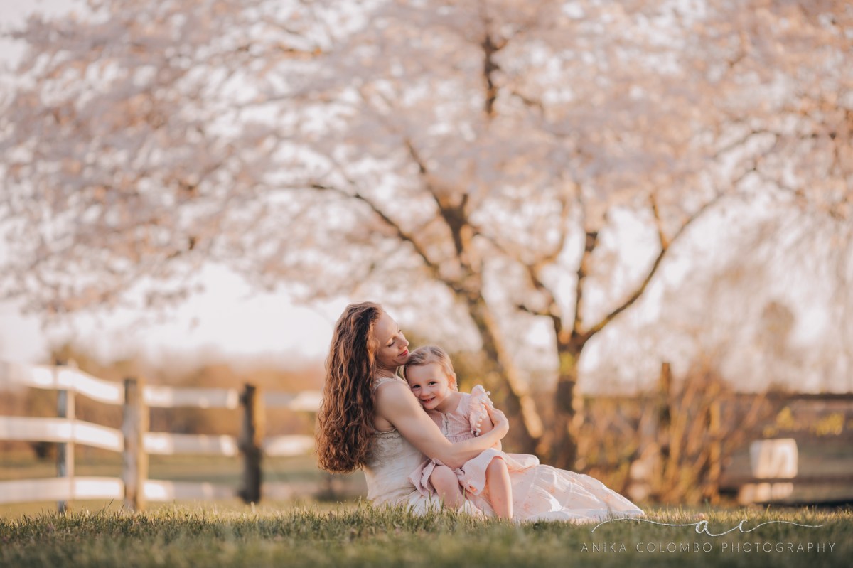 mother holding daughter in a pasture in front of a cherry blossom tree