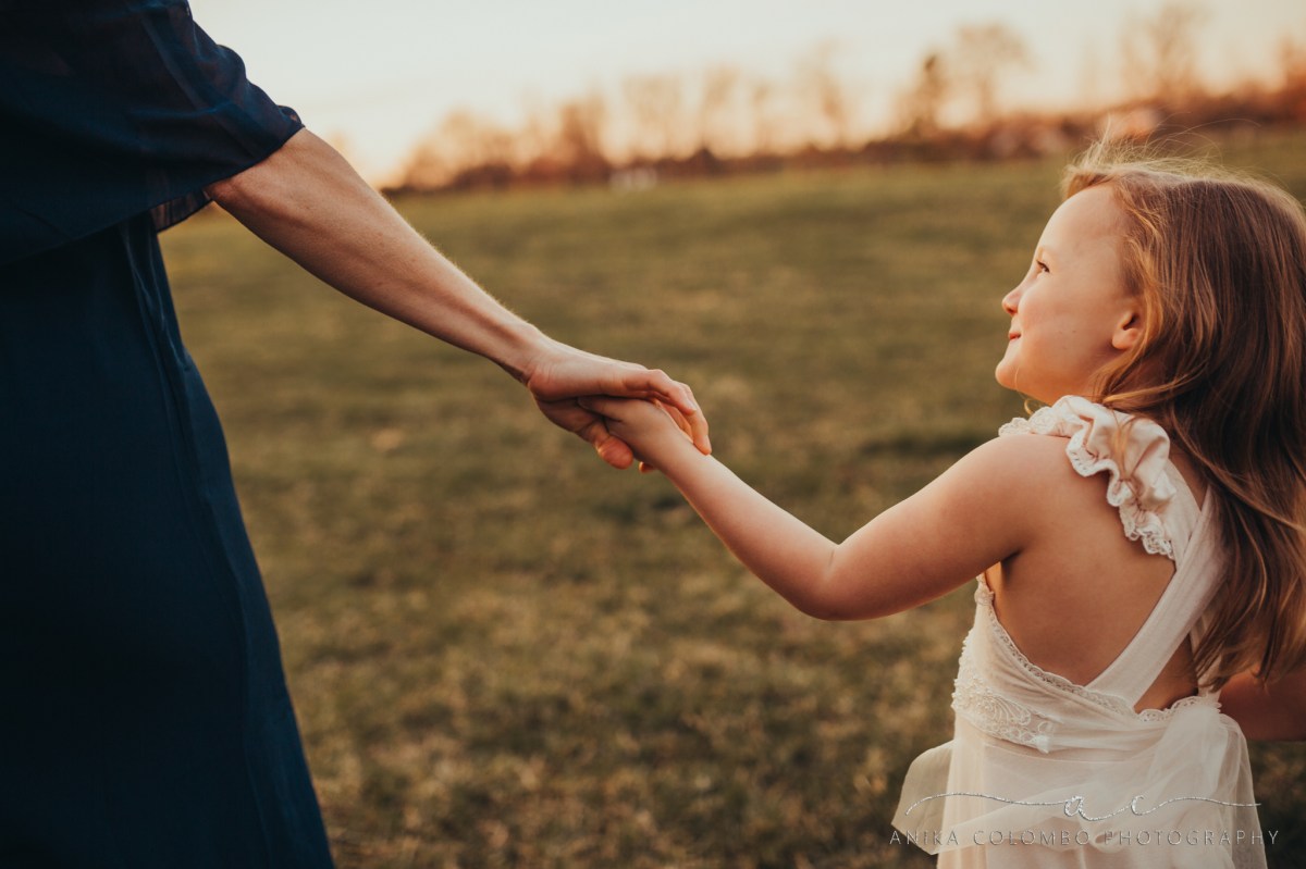 mother holding daughters hand in a field as she looks up smiling at her