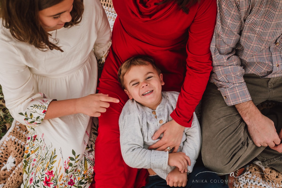 toddler sitting in his mothers lap while family tickles him
