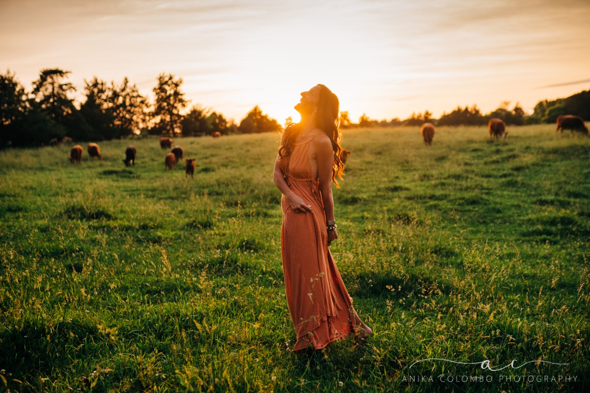 woman standing in a field with cows dancing and laughing while twirling her dress