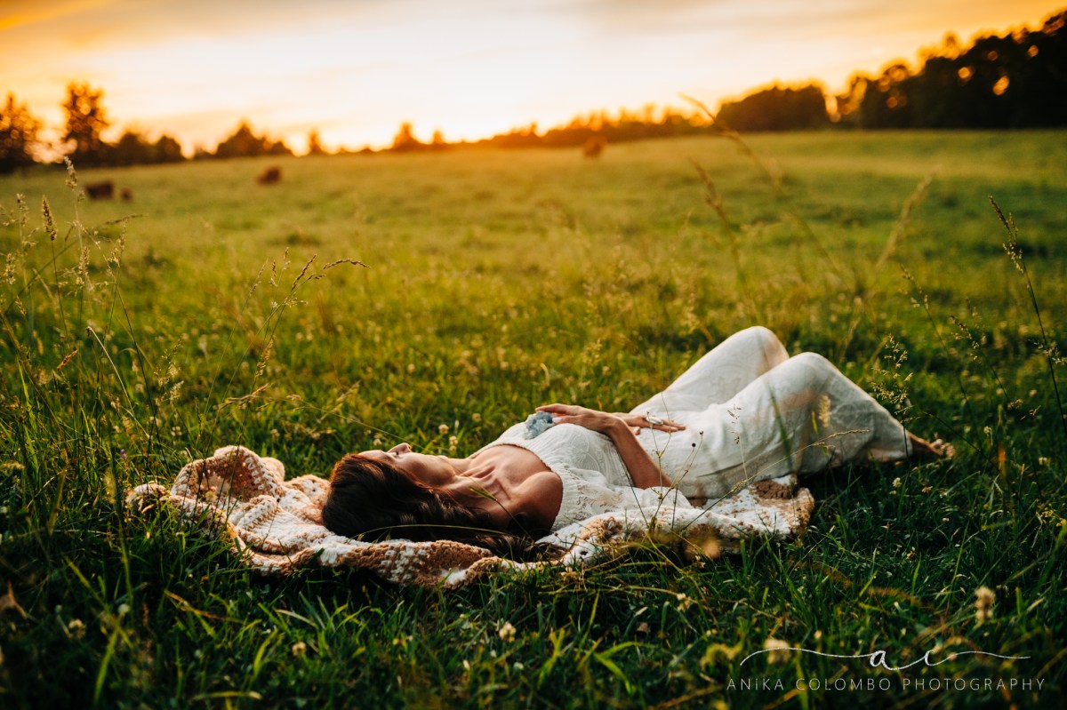 woman laying in a field with cows holding a crystal to her chest
