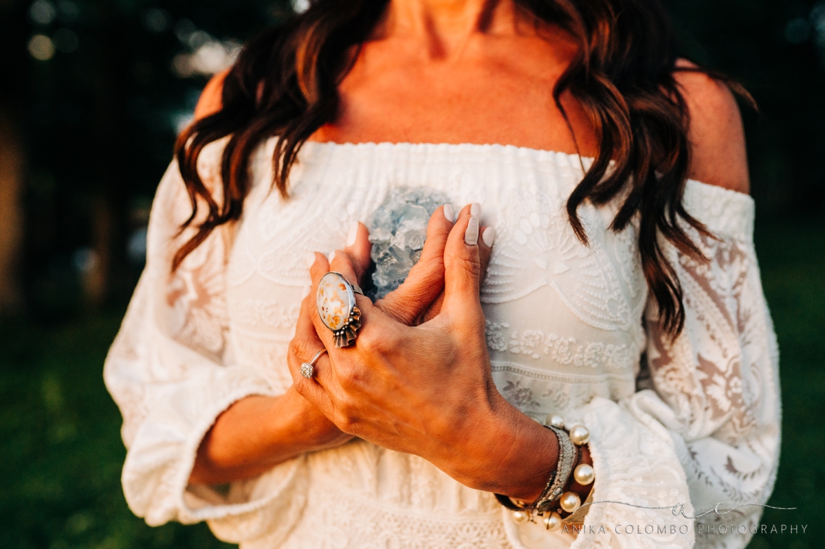 woman in off shoulder dress holding a crystal to her chest with lots of chunky vintage jewelry