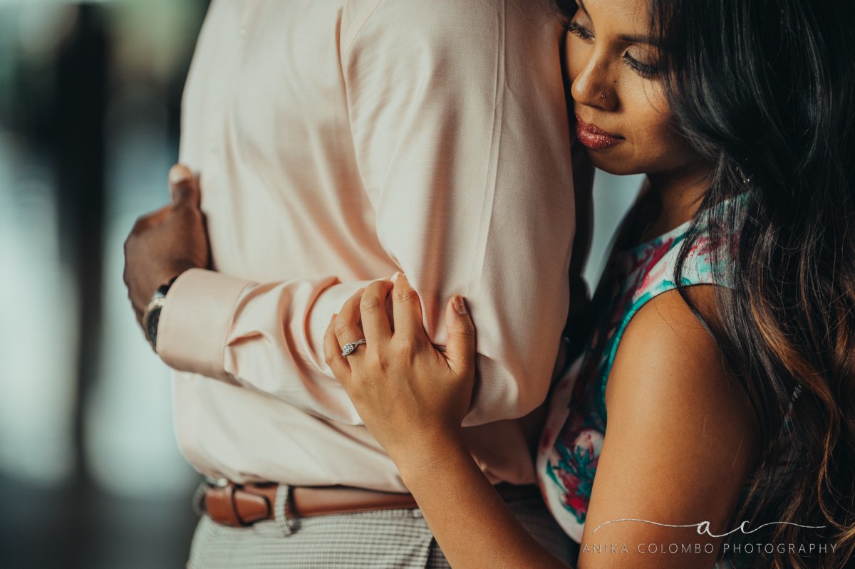 female embracing a man from behind resting her cheek on his back and hand on his elbow