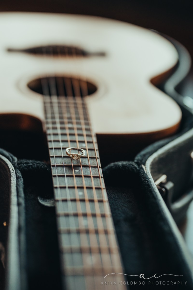 photo of a guitar with an engagement ring sitting on the strings
